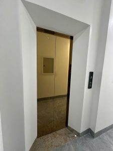 Cửa tầng hai thang máy inox vàng gương đặt trong hố thang xây, bảng gọi tầng hiển thị số, nhà anh Phước Việt Yên