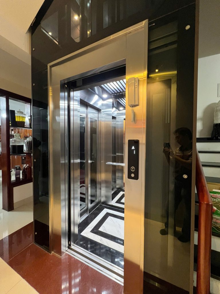 Thang máy kính khung thép Bắc Giang tại nhà chị Hạnh, 168 Nguyễn Khuyến — cabin inox xước, cửa mở nhìn vào sàn đá hoa văn