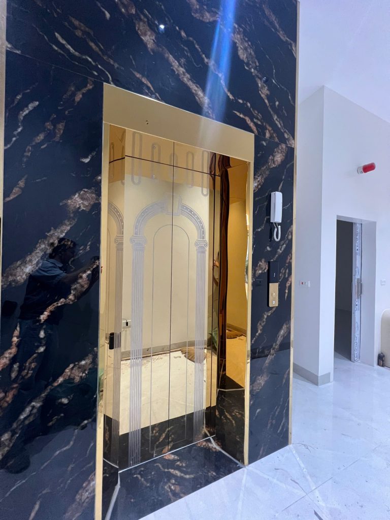 Cửa tầng thang máy phòng khám Bắc Giang ốp inox titan vàng gương ăn mòn hoa văn vòm cột, khung bao đá marble đen tại Nha khoa Minh Thư, Yên Dũng
